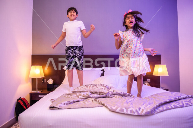 طفلان عربيان خليجيان سعوديان يلعبان فوق السرير، قضاء وقت ممتع، اللعب والمرح، ممارسة انشطة ترفيهية، اجواء عائلية سعيدة 