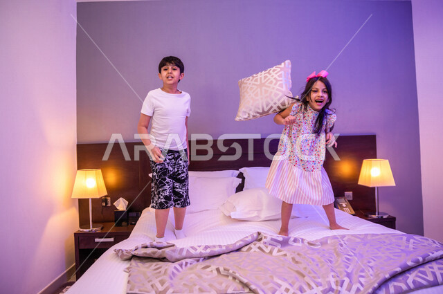 طفلان عربيان خليجيان سعوديان يلعبان فوق السرير، قضاء وقت ممتع، اللعب والمرح، ممارسة انشطة ترفيهية، اجواء عائلية سعيدة 
