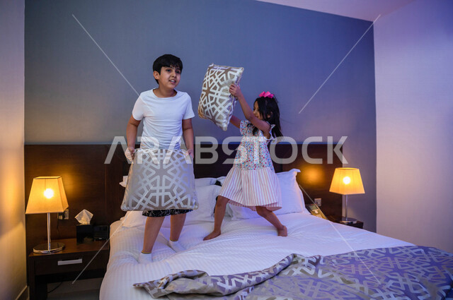 طفلان عربيان خليجيان سعوديان يلعبان فوق السرير، قضاء وقت ممتع، اللعب والمرح، ممارسة انشطة ترفيهية، اجواء عائلية سعيدة 