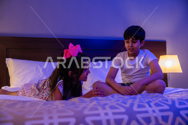 Two Saudi Arabian Gulf children playing on the bed, spending quality time, playing and having fun, engaging in recreational activities, and a happy family atmosphere