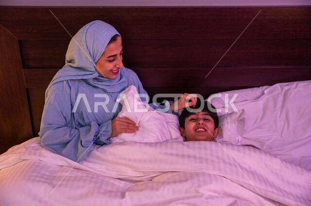 ام عربية خليجية سعودية تطمئن على طفلها، طفل ينام في سرير منعش ومريح على وسادة بيضاء ناعمة، الاسترخاء والاستمتاع بنوم هاديء وصحي