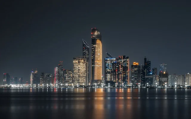 أفق مدينة أبوظبي ليلاً مع انعكاس أضواء ناطحات السحاب