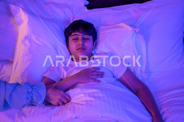 طفل عربي خليجي سعودي نائم، النوم الصحي للاطفال، وقت النوم، النوم المبكر، وسادة بيضاء ناعمة، الاسترخاء والاستمتاع بنوم هادئ وصحي