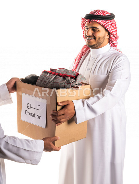 Portrait of a smiling and happy Saudi Arabian Gulf volunteer presenting a charitable basket to a needy Saudi family, distribution of Eid clothes, charitable works, donations and giving, charities for the needy, humanitarian initiatives, the month of Ramad
