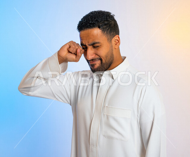 بورتريه لرجل عربي خليجي سعودي يقوم بفرك عينيه بايماءات تدل على الاستيقاظ من النوم ، آلام في العين ،  النعاس والارهاق ، الحاجة الى النوم 