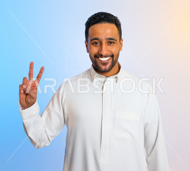 بورتريه لرجل عربي سعودي خليجي مبتسم وسعيد يقوم بايماءات يد تدل على الفوز والإنتصار, تحقيق الاهداف, إنجاز المهام , علامة النصر والقوه