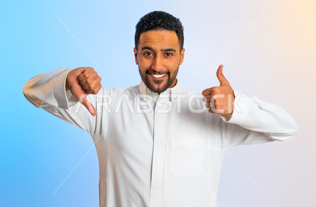 Portrait of a Saudi Arabian Gulf man making hand gestures indicating approval and disapproval, hesitation in something, admiration and dislike, negative and positive evaluation of services, young man raising his thumb up and down