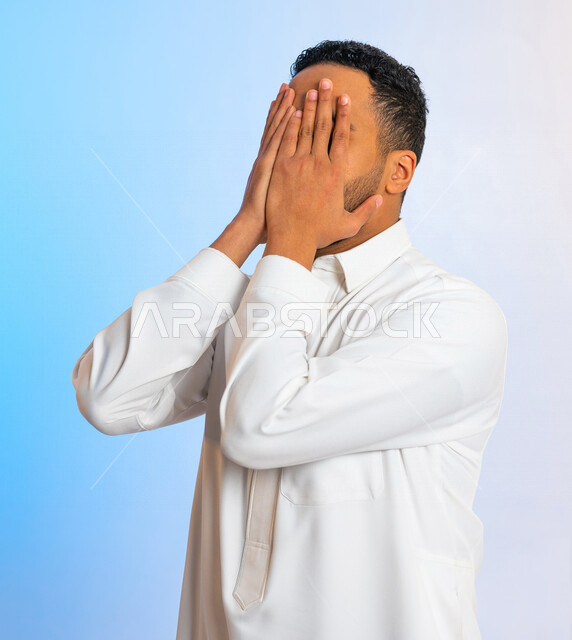 بورتريه لرجل عربي سعودي خليجي يقوم باخفاء وجهه بيديه، ايماءات اليد تدل على الإختباء ، رجل خجول يخفي وجهه بيديه ، منع النظر لشيء ما ، عدم الرؤية