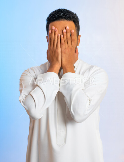 بورتريه لرجل عربي سعودي خليجي يقوم باخفاء وجهه بيديه، ايماءات اليد تدل على الإختباء ، رجل خجول يخفي وجهه بيديه ، منع النظر لشيء ما ، عدم الرؤية
