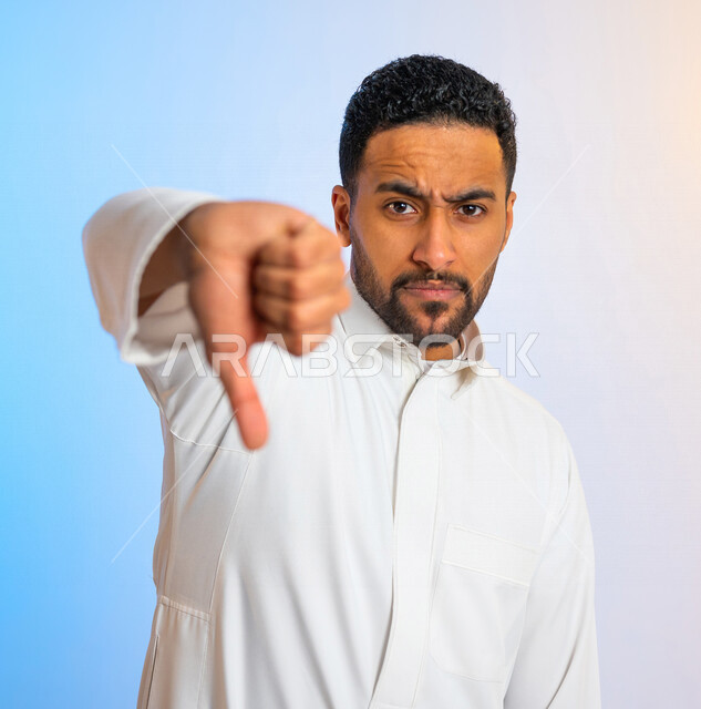 بورتريه لرجل عربي خليجي سعودي يخفض اصبع الابهام، ايماءات يد تدل على عدم اعجابه بشيء ما ، عدم الموافقة ، تقييم سلبي للخدمات ، عدم قبول شيء ما 
