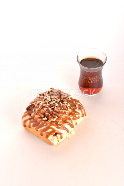 A close-up of a delicious piece of Cinnabon decorated with walnuts and white sauce with a cup of tea, Cinnabon, hot drinks, delicious baked goods, Arabic breakfast, Arabic cafes and restaurants