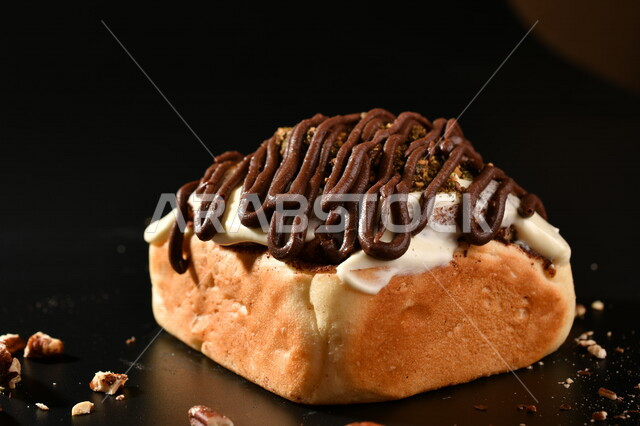Close-up of a delicious cinnabon decorated with walnuts and white sauce, cinnabon, pastries, freshly baked bread, delicious sweets, black background