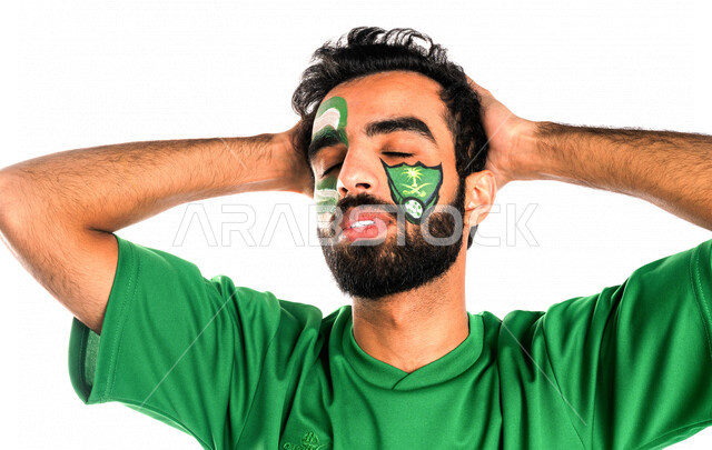 بورتريه لشاب عربي خليجي سعودي يرتدي تيشرت نادي الأهلي السعودي، تشجيع فريق الأهلي السعودي لكرة قدم، متابعة مباراة كرة قدم، شاب يرسم على وجهه شعار نادي الأهلي السعودي، إيماءات وجه ويدين تدل على الدهشة والذهول والخذلان، خلفية بيضاء