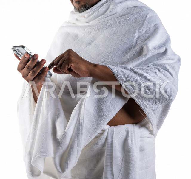 بورتريه لرجل عربي سعودي خليجي يرتدي لباس الاحرام ويستخدم الهاتف المحمول  ، استخدام خدمة تطبيق الارشادات لاداء مناسك الحج والعمرة ، تطبيق مرشد الحج الالكتروني عبر الهاتف المحمول ،  تطبيق الادعية والاذكار 