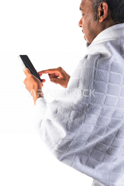 بورتريه لرجل عربي سعودي خليجي يرتدي لباس الاحرام ويستخدم الهاتف المحمول  ، استخدام خدمة تطبيق الارشادات لاداء مناسك الحج والعمرة ، تطبيق مرشد الحج الالكتروني عبر الهاتف المحمول ،  تطبيق الادعية والاذكار 