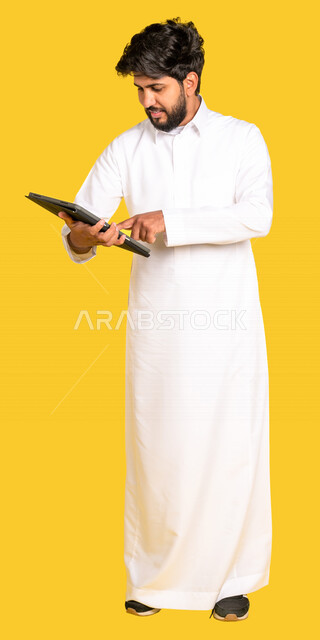 بورتريه لرجل عربي خليجي سعودي يرتدي الزي السعودي يحمل بيده جهاز الحاسوب، رجل أعمال، احتراف وظائف الحاسوب و تكنولوجيا المعلومات، التسويق الالكتروني، تصفح الانترنت، انجاز المهام عبر اللابتوب, صوره للجسم بالطول الكامل, خلفية صفراء
