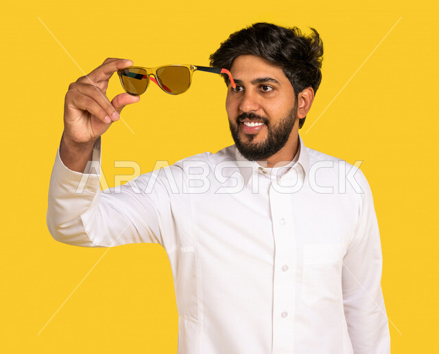 رجل عربي سعودي خليجي يرتدي الزي السعودي, ارتداء النظاره الشمسيه, اختيار نظاره جديده, اقتناء نظارات حماية من الشمس, خلفيه صفراء