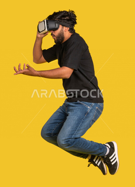 Portrait of a Saudi Arabian Gulf man wearing 3D virtual reality glasses and jumping excitedly, interacting and merging with the virtual world, simulating the virtual world, full length image, full body