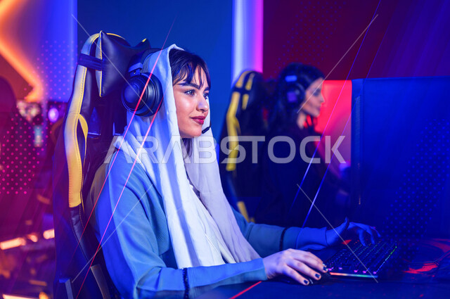 إمرأتان عربيتان سعوديتان خليجيتان ترتديان سماعة الرأس و تلعبان بألعاب الفيديو، اللعب في مقهى العاب الفيديو، المتعة و التسلية باللعب الجماعي، ألعاب الكمبيوتر الترفيهية، اللعب مع الأصدقاء, أنشطه ترفيهيه, تقنيات و ألعاب, خلفيات هولوجراميه ثلاثية الأبعاد