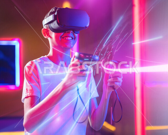 شاب عربي سعودي خليجي يرتدي نظارة العالم الافتراضي, يمسك بيده عصا التحكم و يلعب بألعاب العالم الإفتراضي، المتعة و التسلية بألعاب العالم الإفتراضي, تقنيات و ألعاب, قضاء وقت ممتع, أنشطه ترفيهيه, خلفيات هولوجراميه ثلاثية الأبعاد