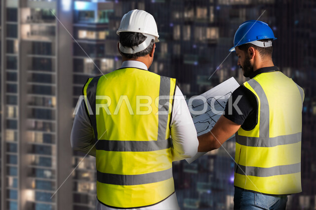 مهندسان معماريان سعوديان خليجيان يناقشان مخطط لمشروع البناء، إرتداء سترة الحماية الخاصة بالعمل, تدقيق العمل، الإشراف والنقاش لمشاريع قيد الانشاء، مفهوم الهندسة المعمارية وادارة المشاريع ، مهن ووظائف هندسية