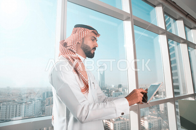 رجل اعمال عربي خليجي سعودي يستخدم جهاز التابلت لمتابعة اعمال الشركة  ، انجاز مهام العمل، نمو الأعمال والتخطيط ، التسويق الالكتروني ، استخدام مواقع التواصل الاجتماعي 