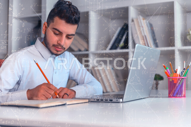 طالب عربي خليجي سعودي يجلس امام الحاسوب المحمول ويدون الملاحظات على الدفتر ، متابعة الدروس والمحاضرات عن بعد ، التعليم الالكتروني ، البحث العلمي ، خلفية لمجموعة من القوانين الرياضية 