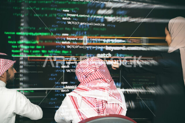 سيدة عربية خليجية سعودية تشير بيدها الى شاشة لغة البرمجة ،فريق عمل يناقش عمل تطوير البرامج ، برمجة المواقع الالكترونية ، تصميم وبناء التطبيقات ، تطوير الويب ، انشاء برامج حاسوبية ، حماية الانظمة والشبكات ، خلفية لغة البرمجة