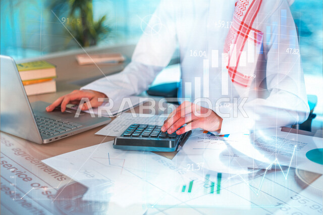 صورة مقربة لرجل عربي خليجي سعودي، يعمل على إدارة الحسابات، إستخدام جهاز الحاسوب المحمول، مهن ووظائف مكتبية، إستخدام الآلة الحاسبة لإجراء العمليات الحسابية، دراسة المشاريع، التوزيع الرقمي والمبيعات، قسم التحليلات والإحصائيات البيانية