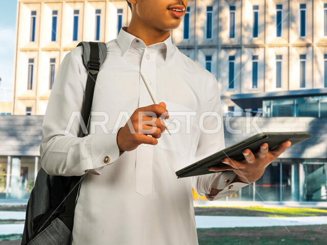 طالب جامعي خليجي سعودي، يحمل بيده جهاز التابلت ويقوم بتسجيل الملاحظات، جامعات ومدارس، التعليم والثقافة، متابعة المحاضرات والدروس اليومية، البحوث العلمية، التعليم الجامعي في المملكة العربية السعودية، التعلم عن بعد، الجد والإجتهاد