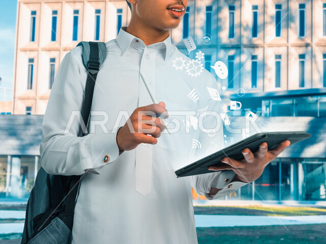 طالب جامعي عربي خليجي سعودي يحمل بيد جهاز التابلت، يقوم بكتابة وتدوين الملاحظات، أيقونات هولوجرامية، المذاكرة للاختبارات الجامعية، مراجعة الدروس اليومية، التعليم الجامعي في المملكة العربية السعودية، كتابة تقارير وأبحاث علمية