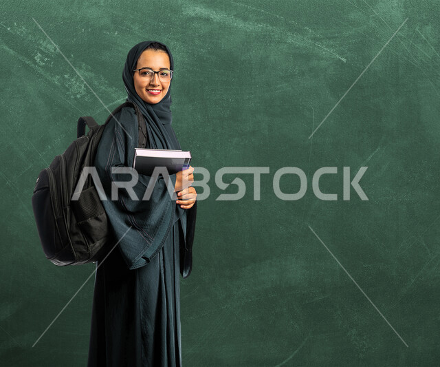  طالبة جامعية عربية سعودية خليجية تحمل الكتب الجامعية، الاستعداد للعام الدراسي الجامعي الجديد، مدارس وجامعات، التعليم الأكاديمي في المملكة العربية السعودية، التعليم والثقافة، مرحلة دراسية، الجد والإجتهاد، لوح سبورة خضراء تعليمية بالخلفية 