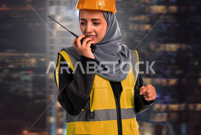 مهندسة عربية خليجية سعودية محجبة، ترتدي خوذة وسترة الحماية الخاصة بالعمل، تحمل جهاز إتصال لاسلكي للتواصل، مفهوم الهندسة المعمارية، إدارة المشاريع الهندسية، مهن ووظائف هندسية، مهندسة معمارية محترفة، اشراف ومتابعة العمل، اعطاء اوامر خاصة بالعمل