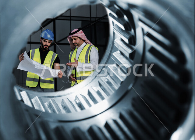 مهندسان معماريان سعوديان خليجيان يناقشان مخطط لمشروع البناء، إرتداء سترة الحماية الخاصة بالعمل، تدقيق العمل، الإشراف والنقاش لمشاريع قيد الانشاء، مفهوم الهندسة المعمارية، إدارة المشاريع الهندسية، مهن ووظائف هندسية، مخططات وتصماميم هندسية