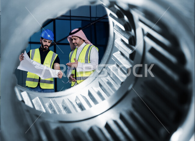 مهندسان معماريان سعوديان خليجيان يناقشان مخطط لمشروع البناء، إرتداء سترة الحماية الخاصة بالعمل، تدقيق العمل، الإشراف والنقاش لمشاريع قيد الانشاء، مفهوم الهندسة المعمارية، إدارة المشاريع الهندسية، مهن ووظائف هندسية، مخططات وتصماميم هندسية