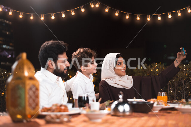 A happy Saudi Gulf family at the breakfast table in Ramadan, a trip full of varieties of Saudi Arabian food, the month of Ramadan, Ramadan Kareem, Ramadan lantern, the atmosphere of the Saudi family in Ramadan, taking a souvenir selfie through a mobile ph