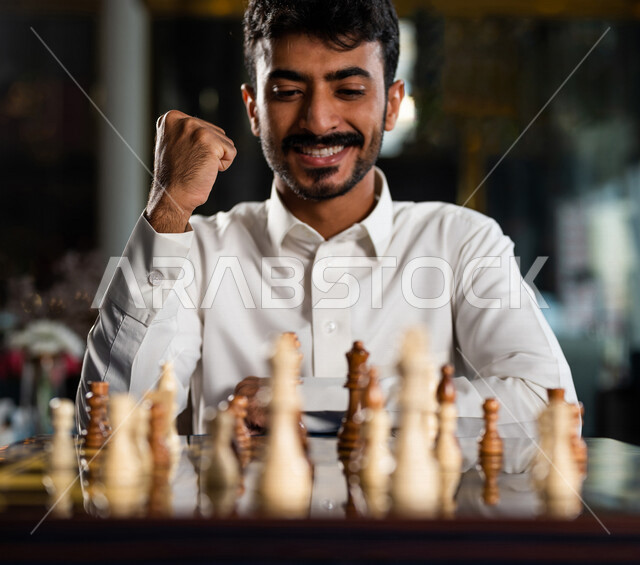 صورة مقربة لشاب عربي سعودي خليجي يلعب لعبة الشطرنج, مفهوم التركيز و التحدي, التخطيط والتفكير, لعبة رقمية استراتيجية على رقعة الشطرنج, إيماءات تدل على الفوز, أنشطه ترفيهيه, قضاء وقت ممتع في اللعب, تسليه وترفيه