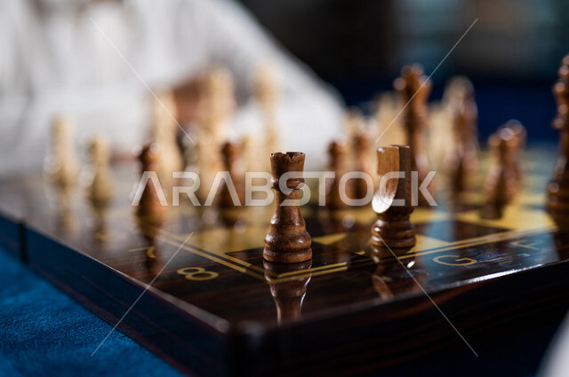 صورة مقربة لشاب عربي سعودي خليجي يلعب لعبة الشطرنج, مفهوم التركيز و التحدي, التخطيط والتفكير, لعبة رقمية استراتيجية على رقعة الشطرنج, أنشطه ترفيهيه, قضاء وقت ممتع في اللعب, تسليه وترفيه