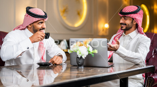زملاء عمل عرب سعوديون خليجيون مجتمعون في المقهى, حوار ونقاش عمل خارج الشركه, انجهاز مهام العمل عبر جهاز الحاسوب, إدارة الأعمال عن بعد, توزيع مهام العمل بين الزملاء,  الإستمتاع بشرب القهوه في متجر القهوه, مقاهي في المملكه العربيه السعوديه