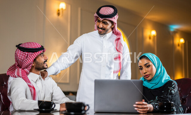 زملاء عمل عرب سعوديون خليجيون مجتمعون في المقهى, حوار ونقاش عمل خارج الشركه, انجاز مهام العمل عبر جهاز الحاسوب, إدارة الأعمال عن بعد, توزيع مهام العمل بين الزملاء,  الإستمتاع بشرب القهوه في متجر القهوه, مقاهي في المملكه العربيه السعوديه