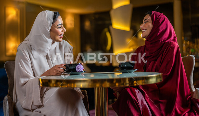 سيدتان عربيتان خليجيتان سعوديتان مبتسمتان تجلسان في المقهى  تقومان بشرب فنجان القهوة الساخنة ، جلسة صداقة ، لقاء و تعارف ، حوار و نقاش ، علاقات إجتماعية ، قضاء أوقات ممتعة 