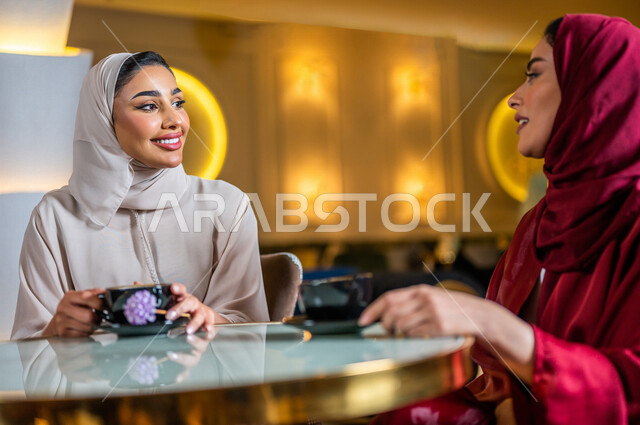 سيدتان عربيتان خليجيتان سعوديتان مبتسمتان تجلسان في المقهى  تقومان بشرب فنجان القهوة الساخنة ، جلسة صداقة ، لقاء و تعارف ، حوار و نقاش ، علاقات إجتماعية ، قضاء أوقات ممتعة 