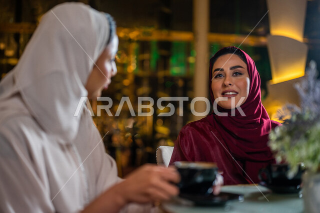 صورة مقربة لسيدة عربية خليجية سعودية تجلس في المقهى مع صديقاتها ، تقومان بشرب فنجان القهوة الساخنة بسعادة ، جلسة صداقة ، لقاء و تعارف ، حوار و نقاش ، علاقات إجتماعية ، قضاء أوقات ممتعة 