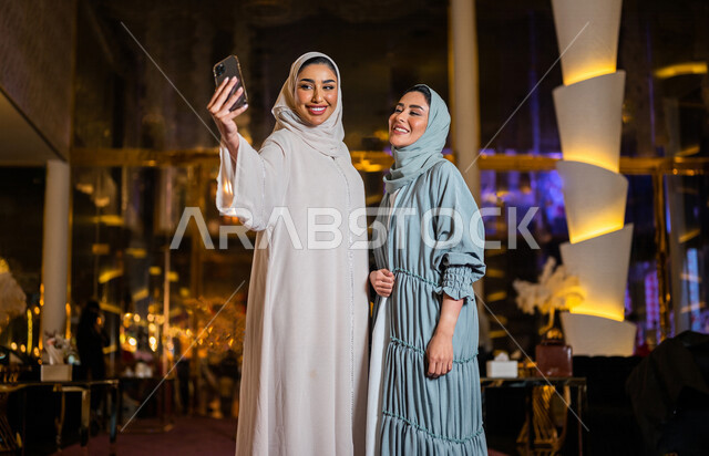 سيدتان عربيتان خليجيتان سعوديتان صديقتان مبتسمتان تقومان بالتقاط صورة سلفي تذكارية عبر الهاتف المحمول ، سياحة و استجمام ، صداقات و تعارف ، علاقات إجتماعية ، قضاء أوقات ممتعة