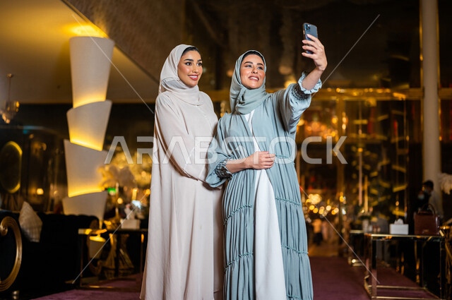 سيدتان عربيتان خليجيتان سعوديتان صديقتان مبتسمتان تقومان بالتقاط صورة سلفي تذكارية عبر الهاتف المحمول ، سياحة و استجمام ، صداقات و تعارف ، علاقات إجتماعية ، قضاء أوقات ممتعة