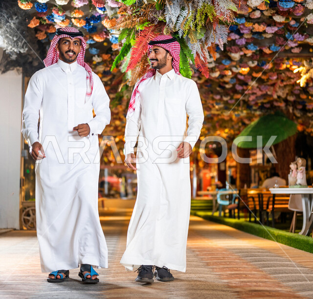 رجلان عربيان خليجيان سعوديان صديقان مبتسمان يسيران معاً في نزهة ممتعة لإحدى الأماكن الترفيهية ، صداقات و تعارف ، علاقات إجتماعية ، كوفي شوب ، قضاء أوقات ممتعة