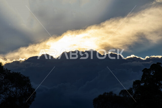صورة ابداعية للغيوم في سماء المملكة العربية السعودية، اشعة الشمس من خلف الغيوم في السماء الزرقاء، مناظر طبيعية، صورة ظلية للنباتات، جمال وروعة السماء الملبدة بالغيوم، الطبيعة في السعودية 