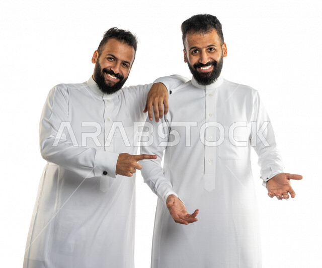 بورتريه لرجلان توأم عربيان خليجيان سعوديان مبتسمان وسعيدان، احدهم يضع شيء على يده والاخر يشير اليه، رفع و حمل شيء، شرح وتوضيح شيء ما، اشاره الامساك، حركة اصبع واشارات، نقاش وحوار، خلفية بيضاء