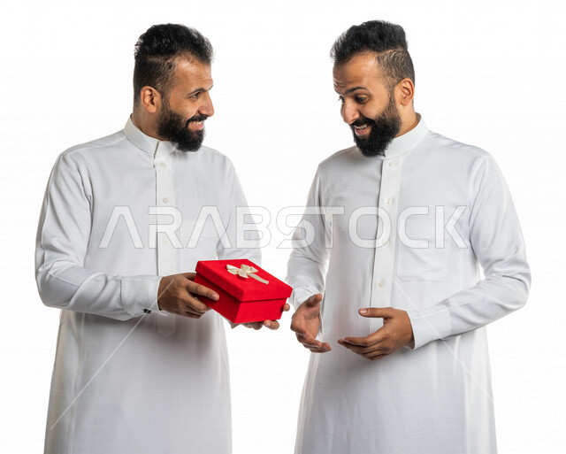 بورتريه لرجل عربي خليجي سعودي يقدم صندوق أحمر لأخاه التوأم بايماءات تدل على الدهشة والسعادة ، هدية عيد ميلاد ، هدايا تذكارية ، المشاركة في الأعياد والإحتفالات ، مناسبات سعيدة