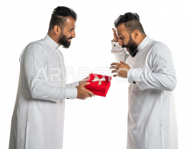 بورتريه لرجل عربي خليجي سعودي يقدم صندوق أحمر لأخاه التوأم بايماءات تدل على الدهشة والسعادة ، هدية عيد ميلاد ، هدايا تذكارية ، المشاركة في الأعياد والإحتفالات ، مناسبات سعيدة